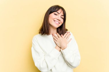 Sarı arka planda izole edilmiş genç beyaz kadın, dost canlısı bir ifadeye sahip, avuçlarını göğsüne bastırıyor. Aşk konsepti.