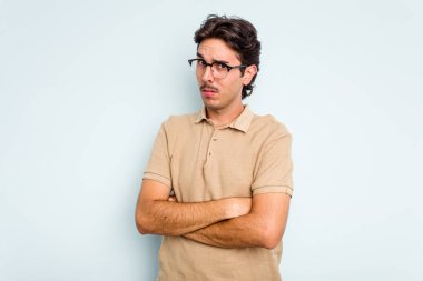 Latin asıllı genç adam mavi arka planda izole edilmiş. Mutsuz bir şekilde kameraya bakıyor. İğneleyici bir ifadeyle..