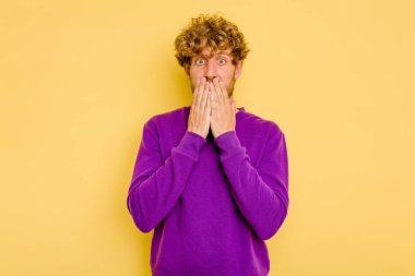 Sarı arka planda izole edilmiş genç beyaz adam elleri endişeli bir şekilde ağzı örtüyor..