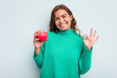 Elmalı genç beyaz kadın mavi arka planda izole edilmiş neşeli ve kendinden emin..