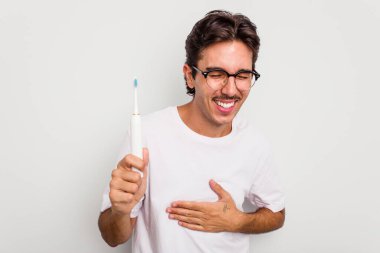 Beyaz arka planda elektrikli diş fırçası tutan İspanyol genç adam gülüyor ve eğleniyor..