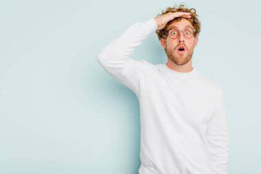 Kafkasyalı genç adam mavi arka planda izole edilmiş, uzaklara bakıyor ve elini alnına koyuyor..