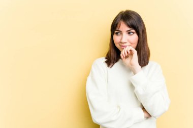 Sarı arka planda izole edilmiş genç beyaz kadın rahatça fotokopi odasına bakan bir şey düşünüyor..