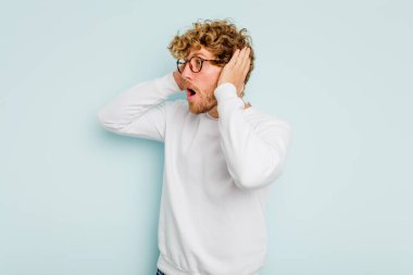 Genç beyaz adam mavi arka planda izole edilmiş bağırıyor, çok heyecanlı, tutkulu, bir şeyden memnun..