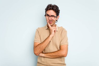 Latin kökenli genç bir adam mavi arka planda izole edilmiş. Bir strateji planlıyor, bir iş yolu düşünüyor..