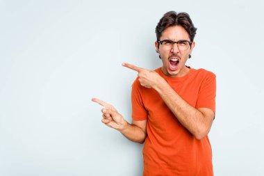 Mavi arka planda izole edilmiş genç İspanyol adam işaret parmaklarıyla fotokopi alanını işaret ederek heyecan ve arzuyu ifade ediyor..