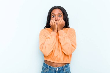 Saçları mavi arka planda izole edilmiş, tırnaklarını yiyen gergin ve endişeli genç Afrikalı Amerikalı bir kadın..