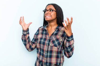 Saçları örgülü genç Afrikalı bir kadın mavi arka planda izole edilmiş, gökyüzüne haykırıyor, yukarı bakıyor, hayal kırıklığına uğramış..