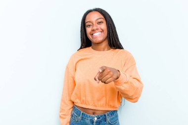 Saçları örülmüş genç Afrikalı Amerikalı bir kadın. Mavi arka planda izole edilmiş. Neşeli gülümsemeler ön tarafı işaret ediyor..