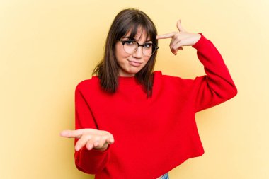 Sarı arka planda izole edilmiş genç beyaz kadın elinde bir ürün tutuyor..