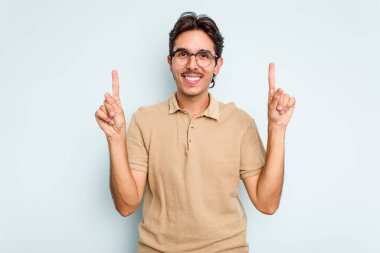 Mavi arka planda izole edilmiş genç İspanyol bir adam iki parmağı da boş bir alan gösteriyor..