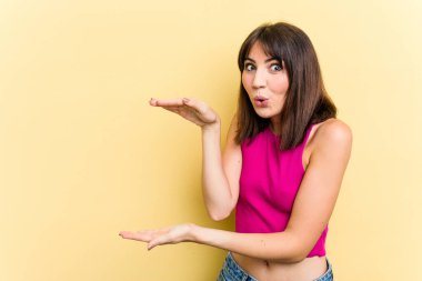 Sarı arka planda izole edilmiş genç beyaz kadın elleri arasında bir kopya alanı tutarken şok ve hayrete düştü..