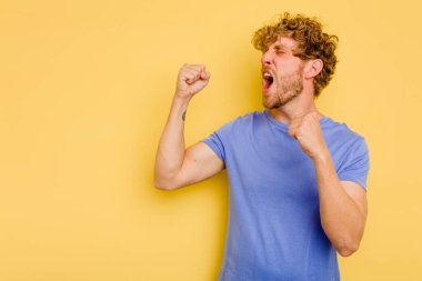 Sarı arka planda izole edilmiş genç beyaz adam zaferden sonra yumruğunu kaldırıyor, kazanan konsept..