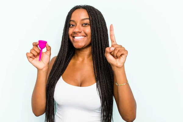 年轻的非裔美国女人拿着月经杯 蓝色背景显示她的手指是第一位的 — 图库照片