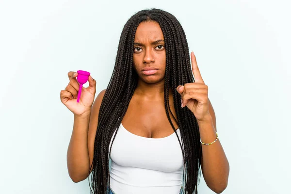 年轻的非洲裔美国女人拿着月经杯 被蓝色背景隔离 手指指向庙宇 专注于一项任务 — 图库照片