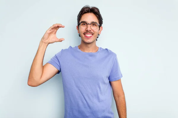 Mladý Hispánec Izolovaný Modrém Pozadí Drží Něco Málo Ukazováčky Usmívá — Stock fotografie
