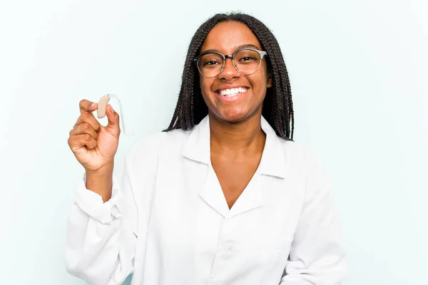 Joven Otorrinolaringóloga Afroamericana Sosteniendo Audífono Aislado Sobre Fondo Azul Riendo — Foto de Stock