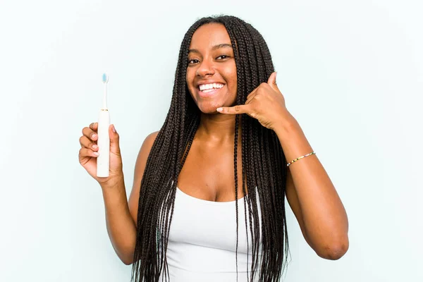 年轻的非洲裔美国妇女手持蓝色背景的电动牙刷 手握手指 摆出打电话的姿势 — 图库照片