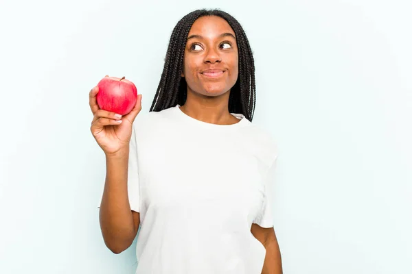 一个年轻的非裔美国女人 拿着一个蓝色背景的苹果 梦想着实现自己的目标和目的 — 图库照片