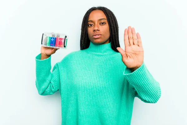 若いアフリカ系アメリカ人の女性がバッテリーボックスを持っています青い背景に隔離されていますストップサインを示す手で立って あなたを防ぎます — ストック写真