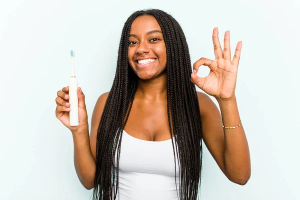 年轻的非洲裔美国女人 手握电动牙刷 蓝色背景 开朗而自信地摆出一副不错的姿势 — 图库照片