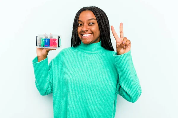 若いアフリカ系アメリカ人女性は青の背景に隔離されたバッテリーボックスを保持指で2番目を示す — ストック写真