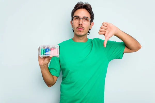 Young hispanic man holding battery box isolated on white background showing a dislike gesture, thumbs down. Disagreement concept.
