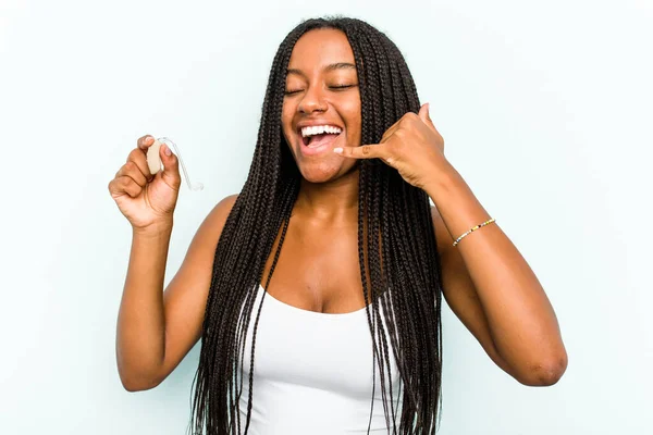 若いアフリカ系アメリカ人女性は青い背景に隔離された補聴器を持っています指で携帯電話のコールジェスチャーを示す — ストック写真