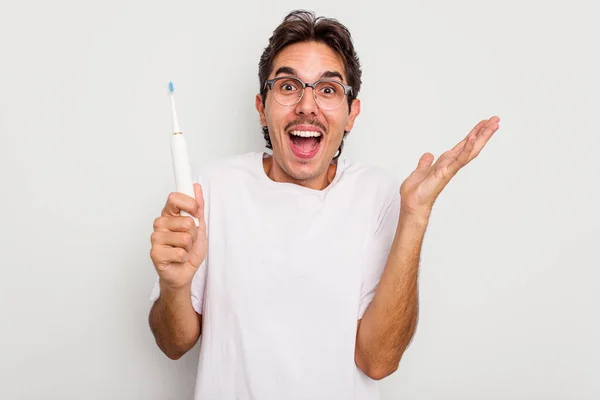 年轻的他的惊慌失措的男人拿着被白色背景隔离的电动牙刷 得到了一个愉快的惊喜 兴奋地举起双手 — 图库照片