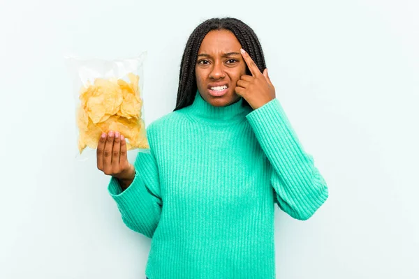 年轻的非洲裔美国女人拿着用蓝色背景隔开的薯片 用食指表示失望的姿态 — 图库照片