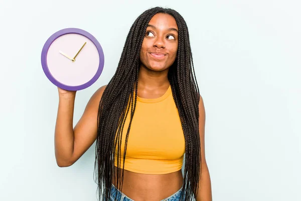 Ung Afroamerikansk Kvinna Som Håller Klocka Isolerad Blå Bakgrund Drömmer — Stockfoto