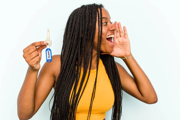 年轻的非洲裔美国女人拿着一把家庭钥匙 在蓝色背景下被隔离 大喊着 手牵着手掌靠近张开的嘴 — 图库照片