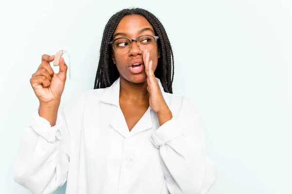 Young African American Otorhinolaryngologist Woman Holding Hearing Aid Isolated Blue Stock Image