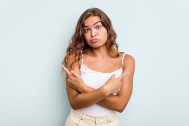 Mavi arka plan noktalarında izole edilmiş genç beyaz kadın iki seçenek arasında seçim yapmaya çalışıyor..