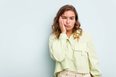 Mavi arka planda izole edilmiş, üzgün ve dalgın hisseden, kopyalama alanına bakan beyaz bir kadın..