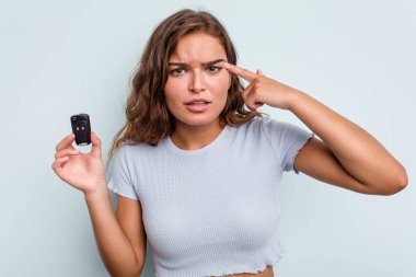 Young caucasian woman holding car keys isolated on blue background showing a disappointment gesture with forefinger.
