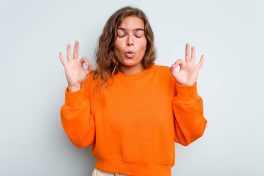 Mavi arka planda izole edilmiş genç beyaz kadın yoğun bir günün ardından rahatlıyor, yoga yapıyor..