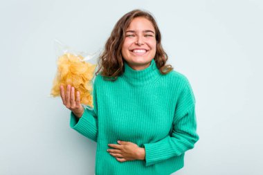 Mavi arka planda patates cipsi tutan beyaz kadın gülüyor ve eğleniyor..