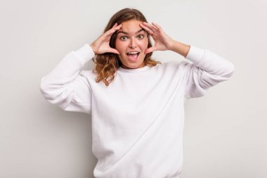 Mavi arka planda izole genç beyaz kadın hoş bir sürpriz alıyor, heyecanlı ve el kaldırıyor..