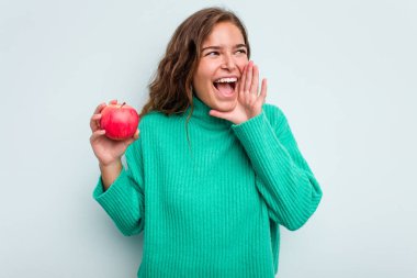 Mavi arka planda izole edilmiş bir elması olan beyaz bir kadın bağırıyor ve avuç içini açık tutuyor..