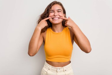 Mavi arka planda izole edilmiş genç beyaz kadın gülümsüyor, parmaklarını ağıza doğrultuyor..