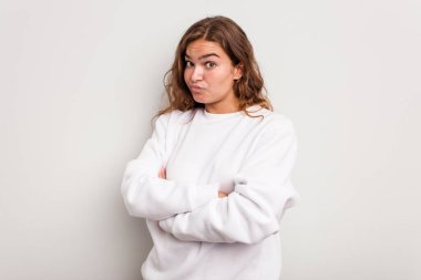 Mavi arka planda izole edilmiş genç beyaz kadın alaycı bir ifadeyle kameraya bakarken mutsuz oluyor..