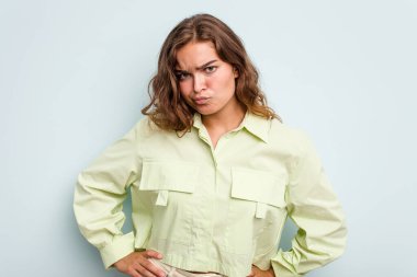 Kafkasyalı genç bir kadın mavi arka planda izole edilmiş, kafası karışmış, şüpheli ve kendinden emin değil..