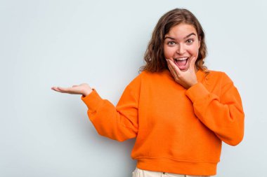 Mavi arka planda izole edilmiş beyaz bir kadın avuç içinde fotokopi alanı tutuyor, el üstünde tutuyor. Şaşırmış ve mutlu..