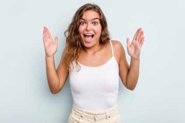 Mavi arka planda izole genç beyaz kadın zaferi ya da başarıyı kutluyor, şaşırıyor ve şok oluyor..