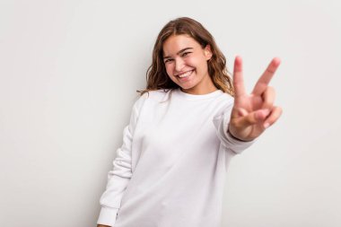 Mavi arka planda izole edilmiş genç beyaz kadın neşeli ve kaygısız parmakları olan bir barış sembolü gösteriyor..