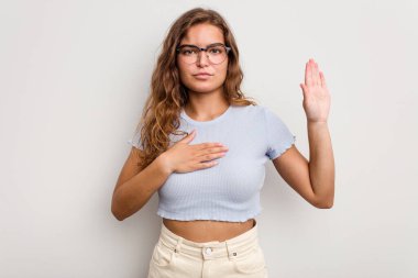 Beyaz bir kadın mavi arka planda izole edilmiş yemin ediyor, elini göğsüne koyuyor..