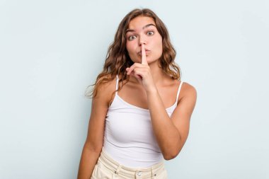 Mavi arka planda izole edilmiş genç beyaz kadın ya sır saklıyor ya da sessizlik istiyor..