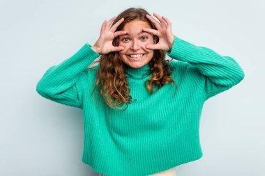 Mavi arka planda izole edilmiş genç beyaz kadın bir başarı fırsatı bulmak için gözlerini açık tutuyor..