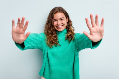 Mavi arka planda izole edilmiş genç beyaz kadın on numarayı elleriyle gösteriyor..